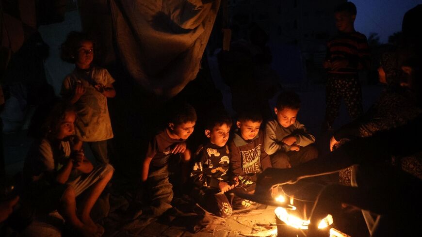 Palestinian children wait for a meal as they sit around a fire in the Bureij camp for Palestinian refugees in the central Gaza Strip