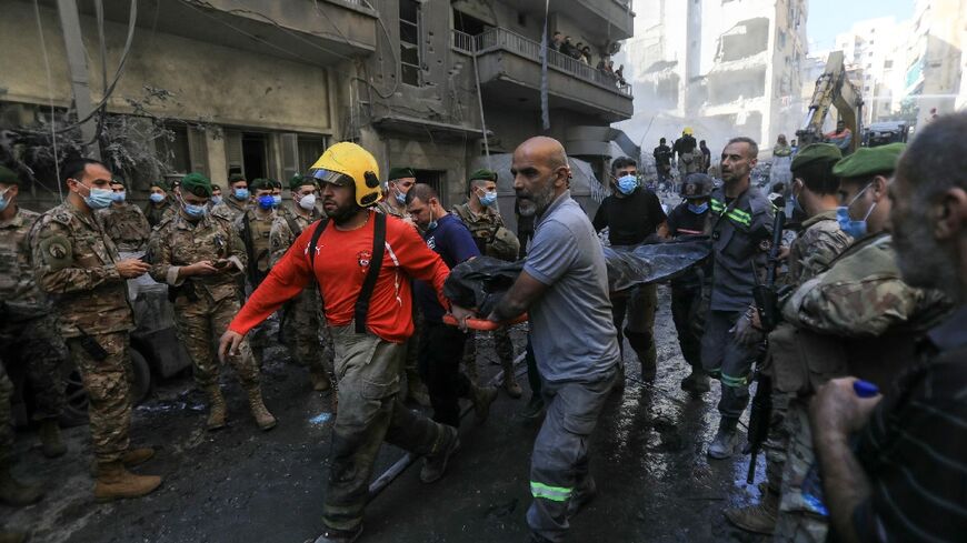 Lebanese soldiers look on as rescuers remove a body extracted from the rubble of a levelled building in Basta