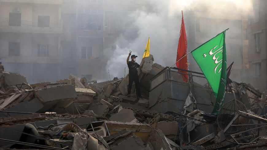 A man poses with Hezbollah banners on the rubble of a building flattened by a pre-dawn Israeli air strike on the Mreijeh district of Beirut’s southern suburbs