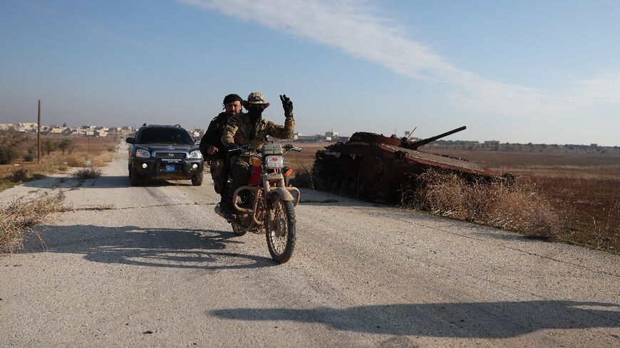 Fighters pass a damaged Syrian Army tank in Miznaz, Syria, which was taken over by jihadists and their Turkish-backed allies in battles with government forces in Aleppo province