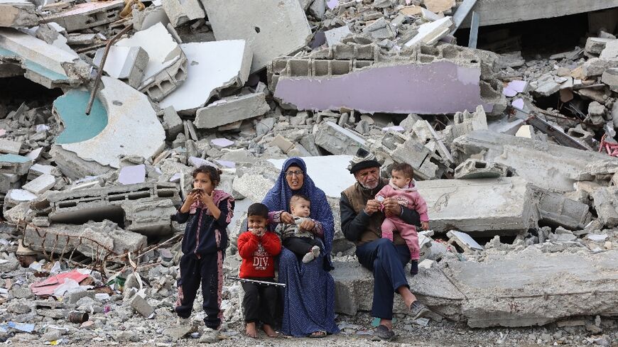 A Palestinian family rests beside the rubble of a shattered building west of Gaza City