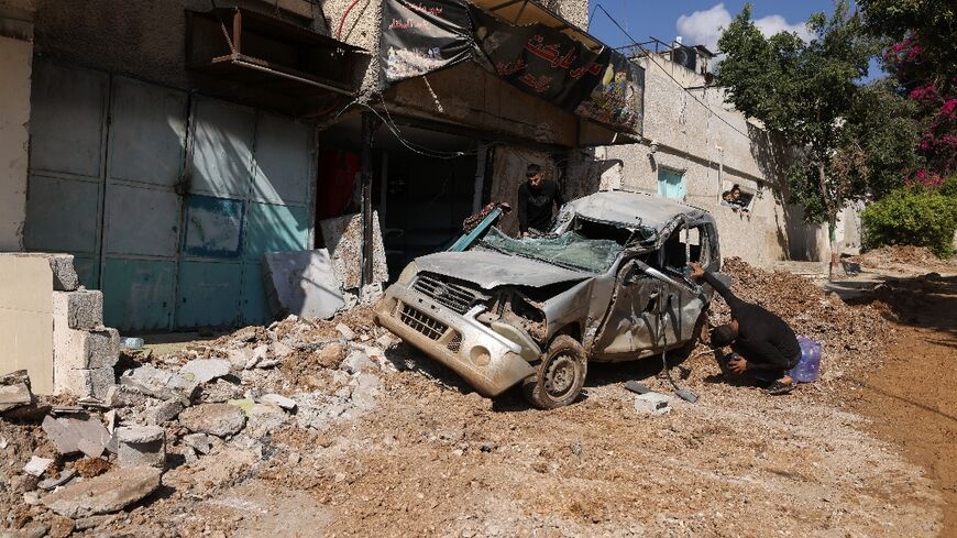 People inspect a destroyed car following an Israeli raid at the Al-Fara refugee camp north of Nablus in the occupied West Bank