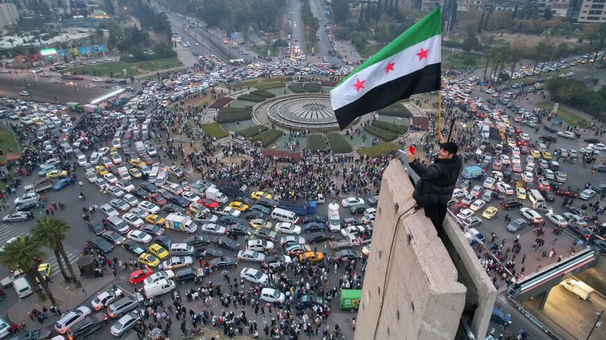 TOPSHOT - An aerial view shows a Syrian man waving the independence-era Syrian flag at Damascus' central Umayyad Square on December 11, 2024. (Photo by Bakr ALKASEM / AFP) (Photo by BAKR ALKASEM/AFP via Getty Images)