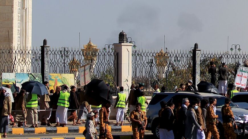 People and security forces watch smoke billowing near a rally in support of Palestinians after Israeli airstrikes on Yemen's Huthi-held capital Sanaa