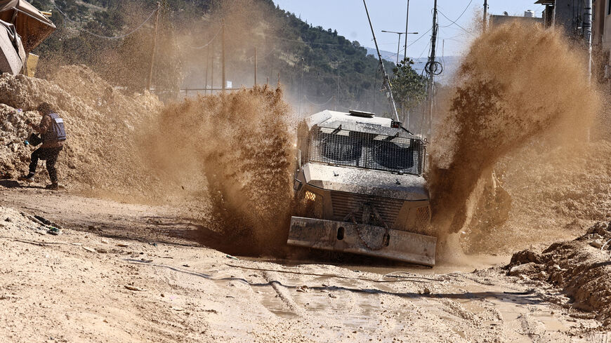 A journalist tries to avoid mud splatter as Israeli forces drive on a destroyed road in the Nur Shams camp for Palestinian refugees near Tulkarem, after reportedly issuing demolition notifications for several houses amid a weeks-long offensive in the occupied West Bank on February 26, 2025. (Photo by Zain JAAFAR / AFP) (Photo by ZAIN JAAFAR/AFP via Getty Images)