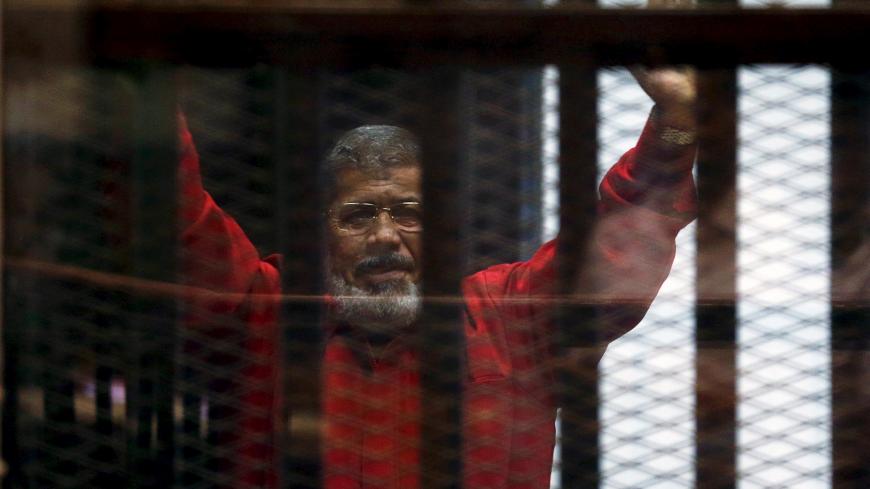 Deposed President Mohamed Mursi greets his lawyers and people from behind bars at a court wearing the red uniform of a prisoner sentenced to death, during his court appearance with Muslim Brotherhood members on the outskirts of Cairo, Egypt, June 21, 2015. REUTERS/Amr Abdallah Dalsh/File Photo - S1AETCRHIPAB