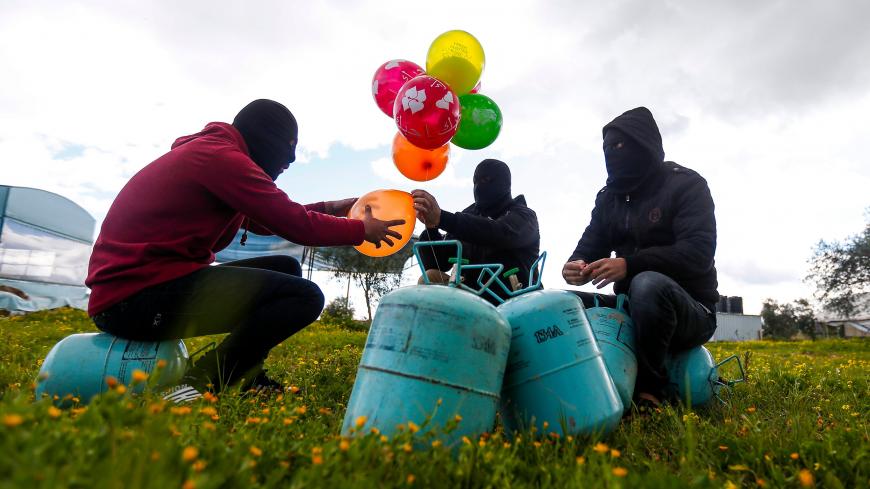 Masked Palestinians prepare to attach balloons to a gas canister before releasing it near Gaza's Bureij refugee camp, along the Israel-Gaza border fence, on February 10, 2020. (Photo by MAHMUD HAMS / AFP) (Photo by MAHMUD HAMS/AFP via Getty Images)