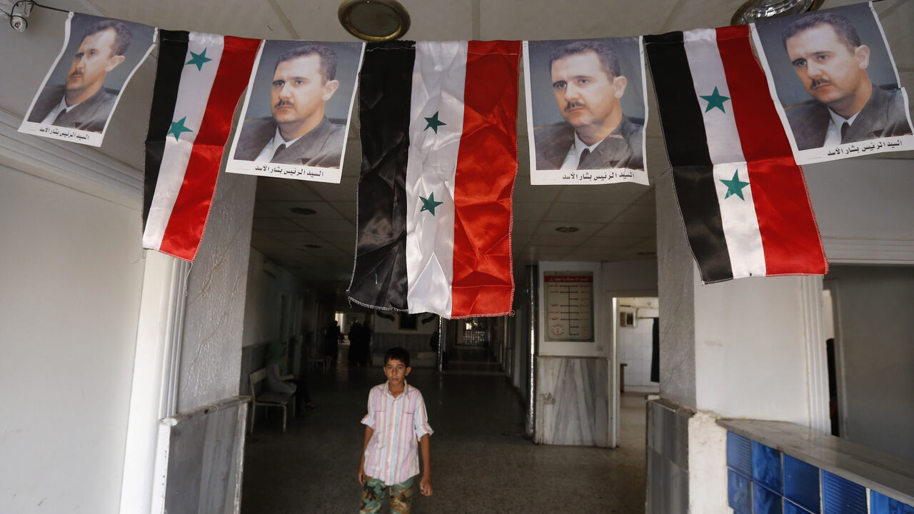 A Syrian boy walks under portraits of Syrian President Bashar al-Assad adorning a hospital in the eastern city of Deir Ezzor on Sept. 20, 2017. 