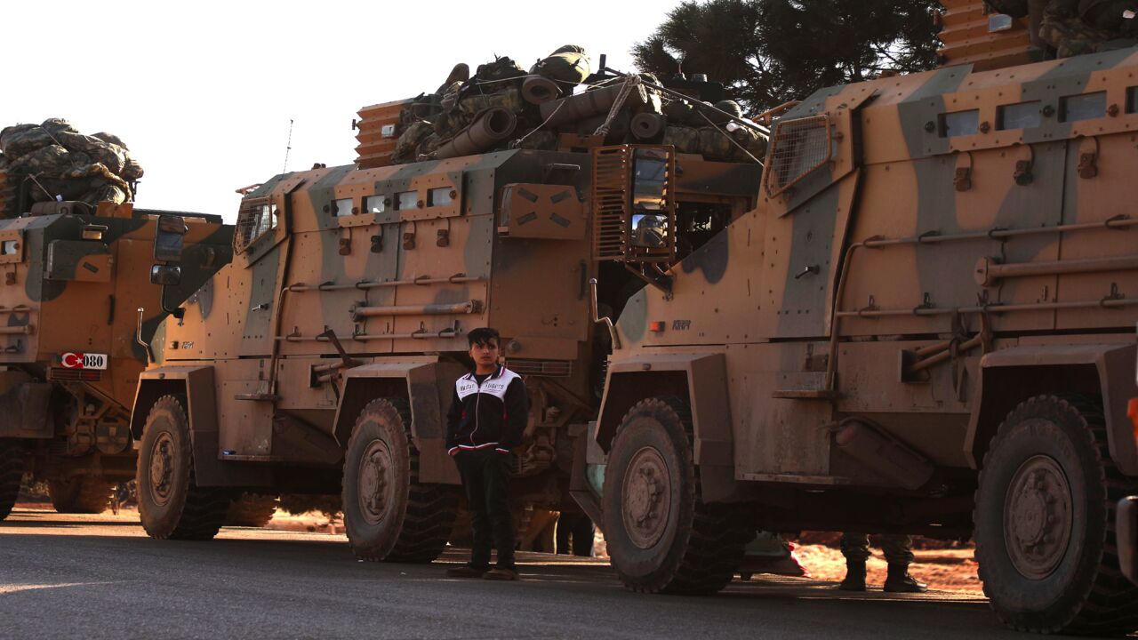 A displaced Syrian boy stands next to Turkish military vehicles near the town of Batabu on the highway linking Idlib to the Syrian Bab al-Hawa border crossing with Turkey, on March 2, 2020.