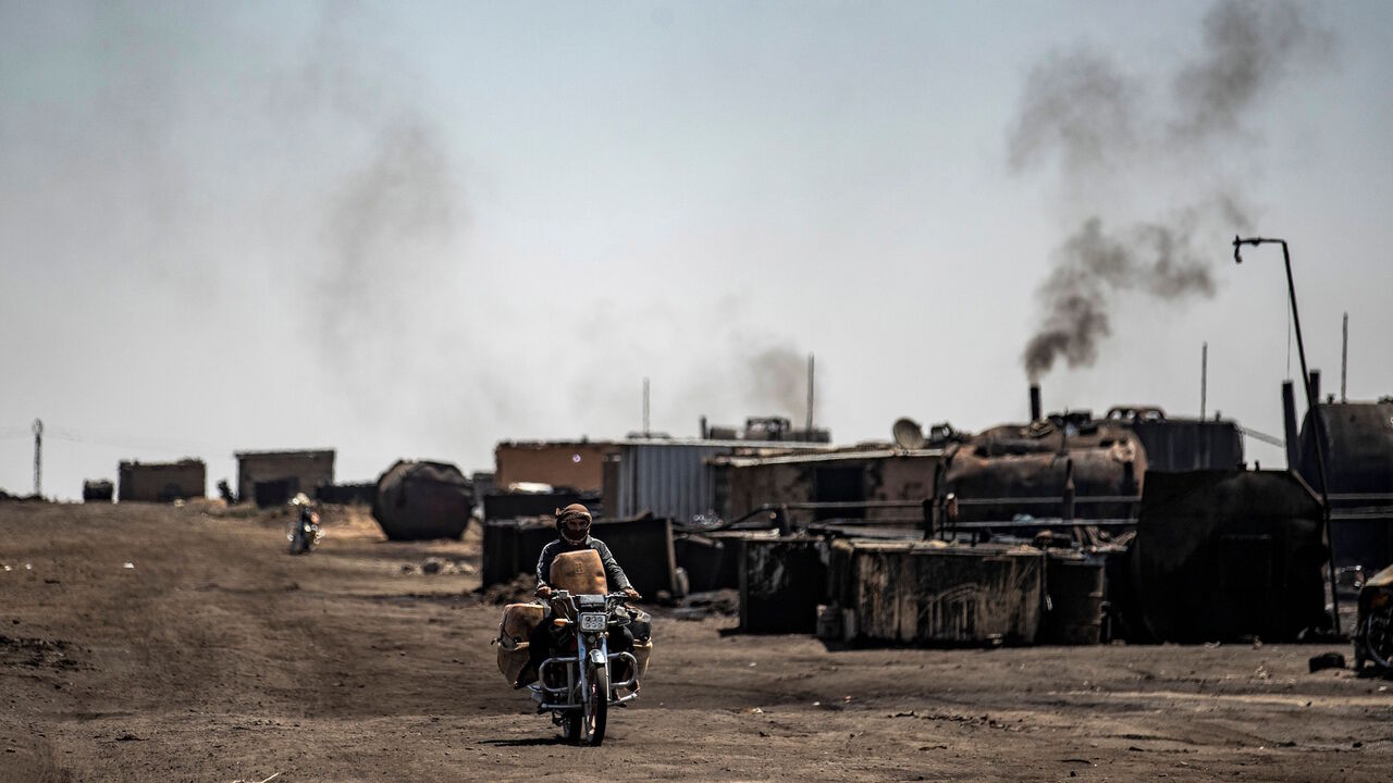 A man drives a motorcycle past a makeshift refinery using burners to distill crude oil in the village of Bishiriya in the countryside near the town of Qahtaniya west of Rumaylan (Rmeilan) in Syria's Kurdish-controlled northeastern Hasakeh province, on July 19, 2020. 