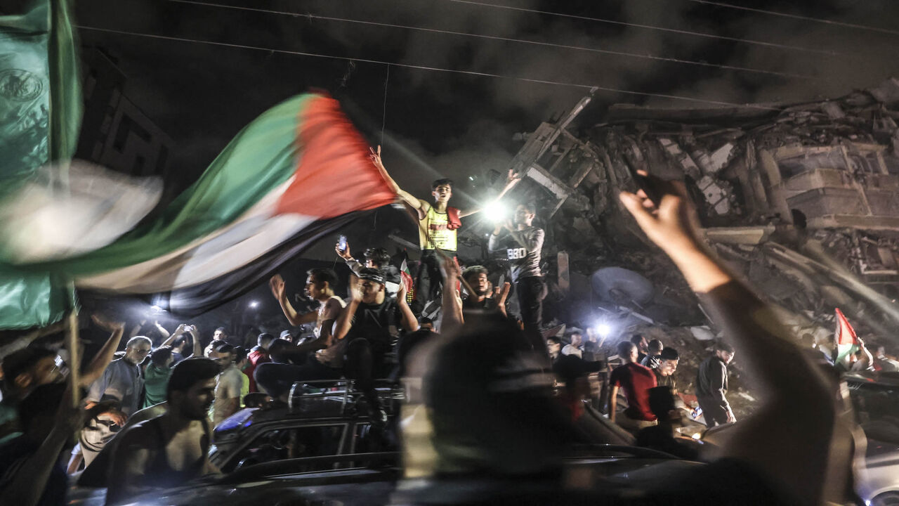 People wave the Palestinian flag as they celebrate in front of a destroyed building in Gaza City early on May 21, 2021, following a cease-fire brokered by Egypt between Israel and the ruling Islamist movement Hamas in the Gaza Strip.