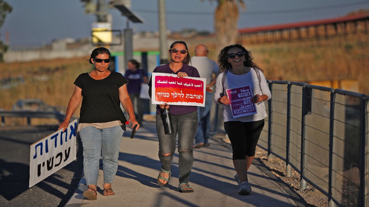 A woman (C) walks with a sign reading in Arabic (top) and Hebrew (bottom) a quote from the Torah's book of Leviticus, "Love your neighbor as yourself," as another (R) holds up one reading bilingually "Together against hate" and another (L) with a sign reading "Unity now," during a demonstration for coexistence between Jews and Arabs in the town of Rosh Pinna in northern Israel on May 13, 2021. 