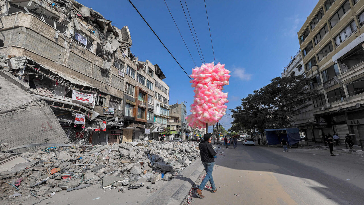 A Palestinian pedlar walks with bags of cotton candy past the rubble of a building destroyed during the May 2021 conflict between Hamas and Israel in al-Rimal neighborhood, Gaza City, Gaza Strip, June 10, 2021.