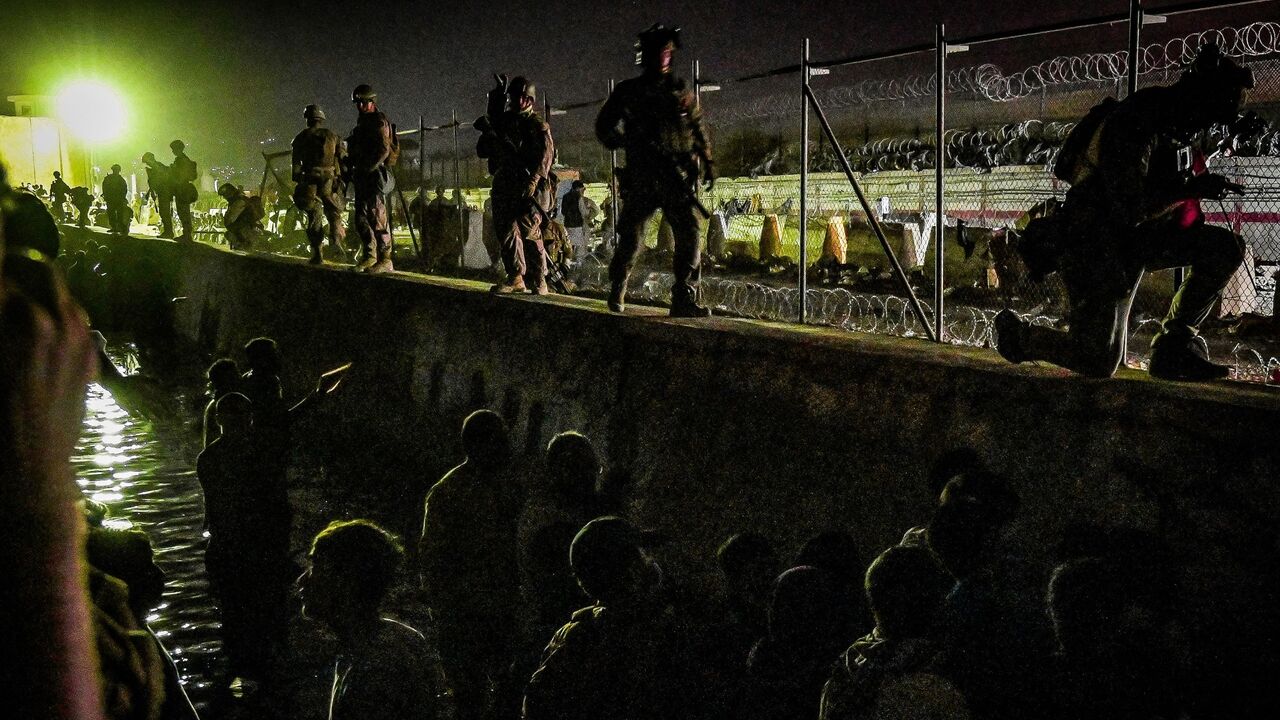 British and Canadian soldiers stand guard near a canal in the late hours of Aug. 22, 2021, as Afghans wait outside the foreign military-controlled part of the airport in Kabul