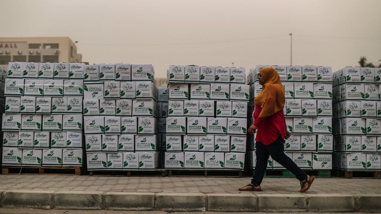 An Egyptian woman walks past cartons with foodstuffs outside a center of nongovernmental organization Egyptian Food Bank on April 05, 2020, in the Egyptian capital, Cairo.