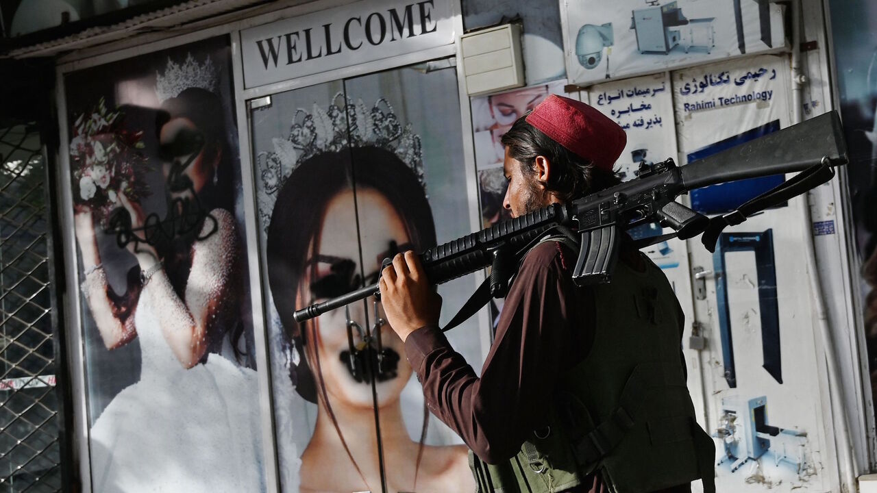A Taliban fighter walks past a beauty salon with images of women defaced using spray paint in Shar-e-Naw in Kabul on Aug. 18, 2021. 