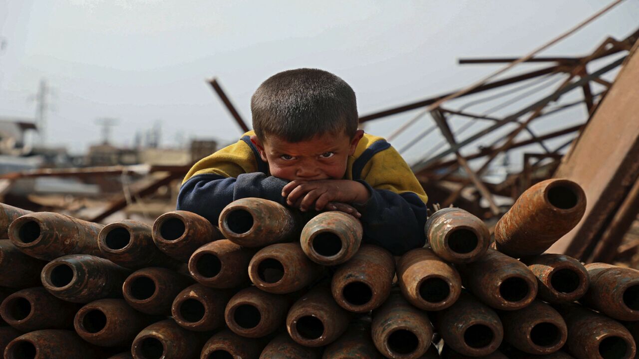 A Syrian child poses atop a stack of neutralized shells at a metal scrapyard on the outskirts of Maaret Misrin town in the northwestern Idlib province, on March 10, 2021.