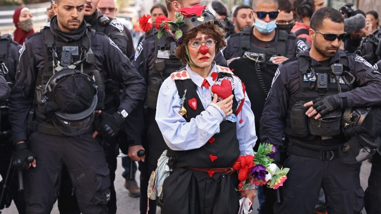 A protester dressed as a clown stands before Israeli police during a demonstration in the flashpoint neighbourhood of Sheikh Jarrah in Israeli-annexed east Jerusalem on February 18, 2022