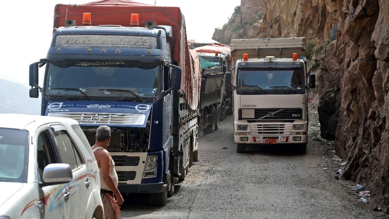 Trucks travel along a heavily damaged road, the only route between Yemen's cities of Taez and Aden