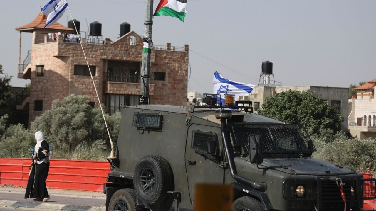 A military vehicle flies an Israeli flag past a lamp post displaying a Palestinian flag in the town of Huwara near Nablus in the occupied West Bank, on May 30, 2022