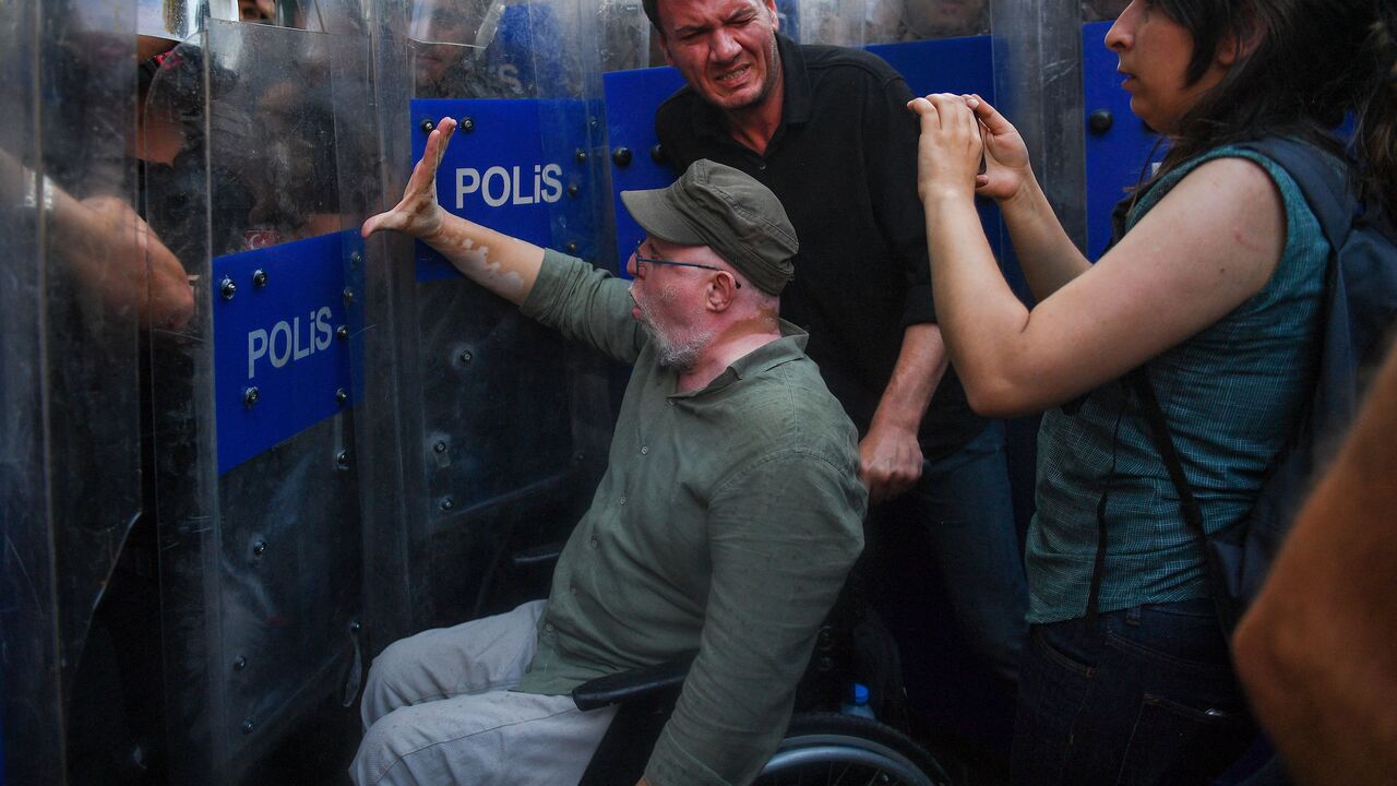 TOPSHOT - Deputy of HDP (People's Democratic Party) Musa Piroglu (L) in a wheelchair tries to stop Turkish riot policemen near Taksim square in Istanbul on May 31, 2022, as the police blocked the access to the square during the ninth anniversary of the Gezi park and Taksim square demonstrations. - People gathered on May 31, 2022 to mark the ninth anniversary of Gezi park at Taksim square. In 2013, what started as a small campaign to save the Gezi Park from the bulldozers eventually drew an estimated three m
