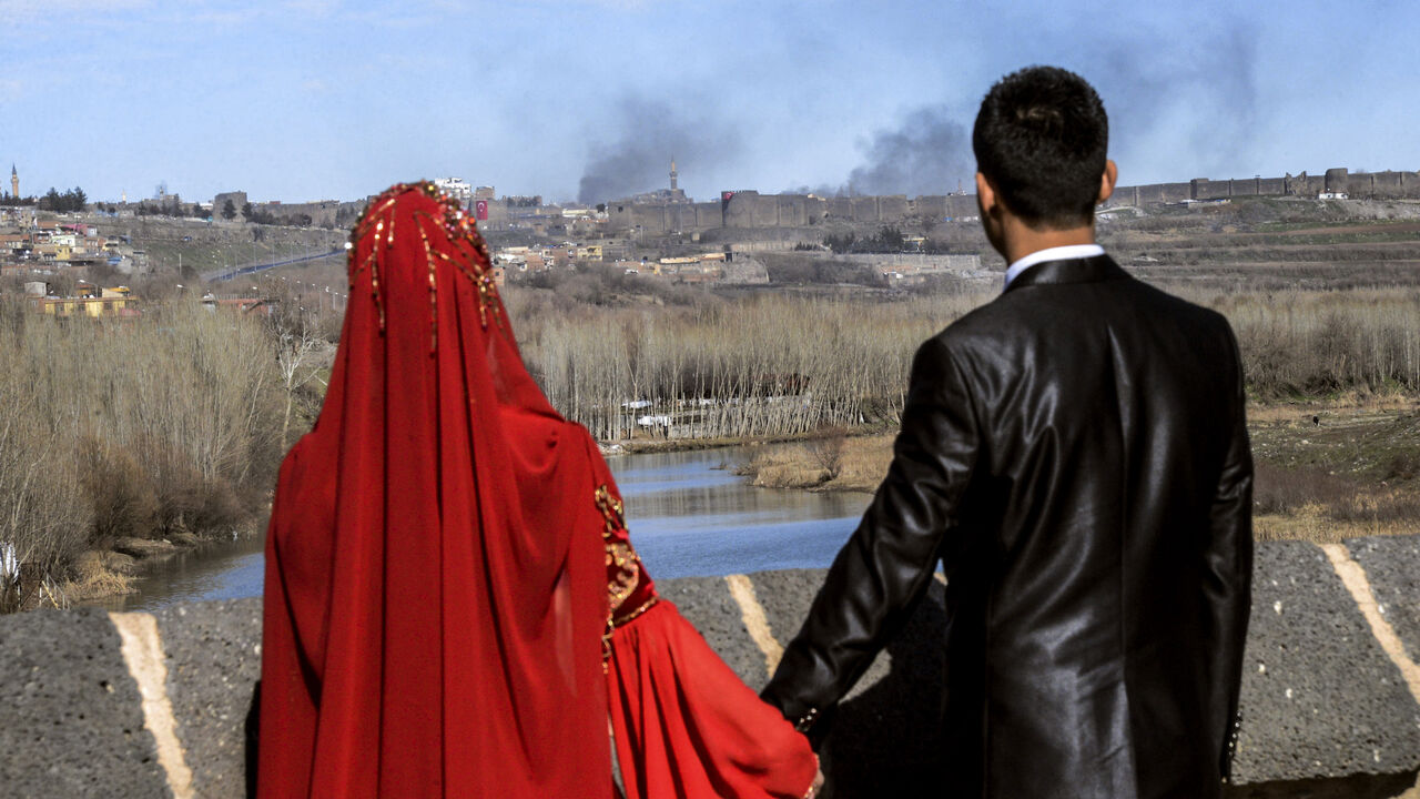 A couple holds hands for a wedding photo as they look at smoke rising over the district of Sur in Diyarbakir.
