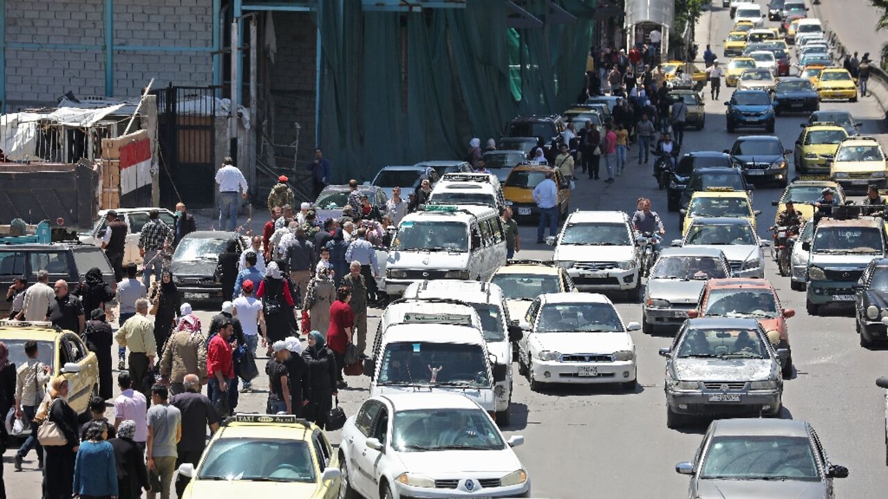 In this file photo taken on May 10, 2020, pedestrians walk along a line of cars in a busy street in the Syrian capital Damascus