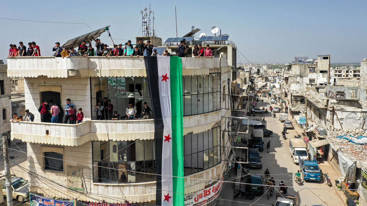 An aerial view of protesters raising a giant flag of the Syrian rebels atop a building during a demonstration against Russia's invasion of Ukraine, Binnish, Idlib province, Syria, April 1, 2022.