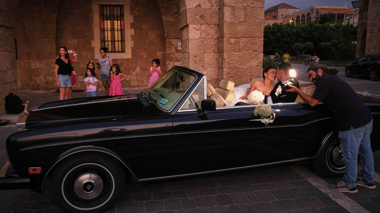 A photographer takes pictures of a newly wedded couple in a classic car, in front of the Saint Estephan Maronite Church at the fishermen's port in Batroun, Lebanon, Aug. 6, 2022.