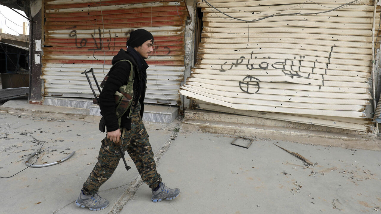 A fighter from the Syrian Democratic Forces (SDF) walks past shops with their fronts painted with the Arabic phrases "beware a sniper" and "caliphate state," after the Kurdish-led and US-backed SDF retook the city from Islamic State fighters, Hajin, Deir ez-Zor province, Syria, Jan. 27, 2019.