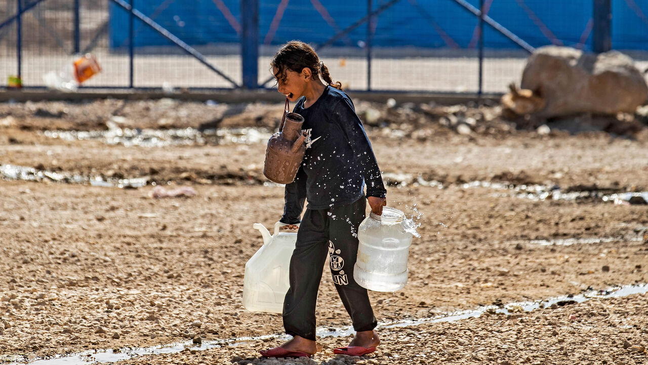 A girl walks while holding water containers in her hands and mouth at the Washukanni camp for the internally displaced near the town of Tuwaynah, near the city of Hasakah, Syria, Oct. 8, 2020.