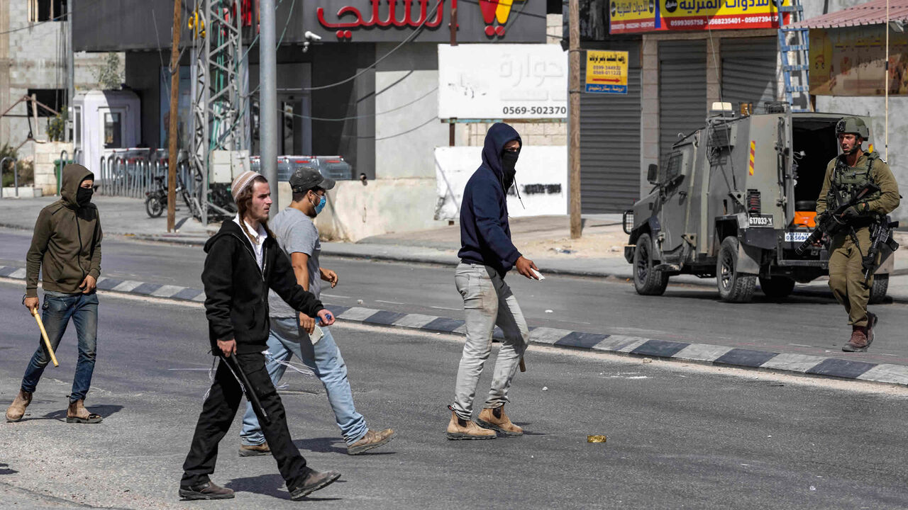 Israeli settlers walk with batons as they cross a street during clashes in which Israeli settlers attacked Palestinian residents and shops in the town of Huwara, West Bank, Oct. 13, 2022.