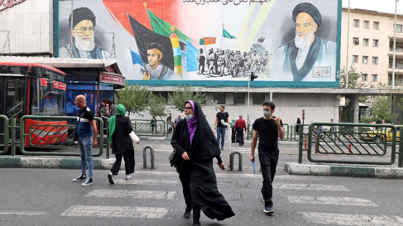 Iranians pass a billboard showing Iran's supreme leader Ayatollah Ali Khamenei and Ayatollah Ruhollah Khomeini (R) in Tehran, before the anti-regime protest movement began in September 2022