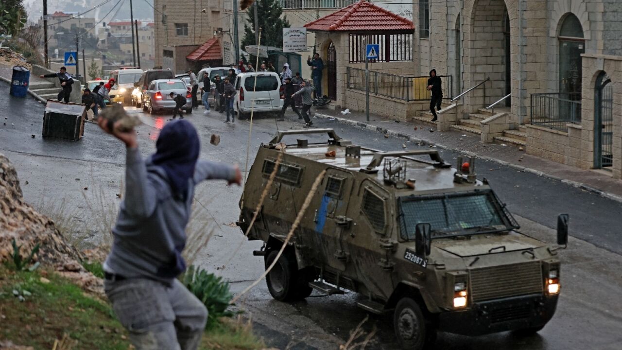A Palestinian hurls a stone at an Israeli military vehicle during a dawn incursion by the army into the West Bank city of Nablus