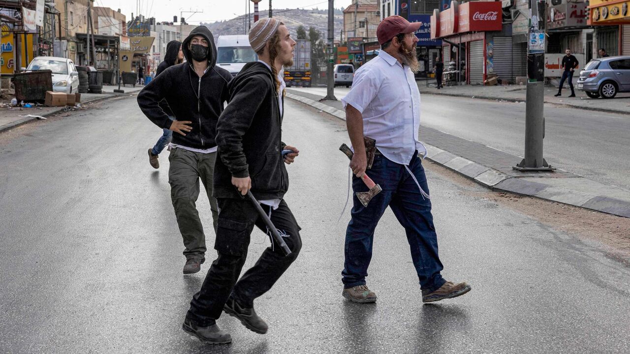 Israeli settlers walk with batons and axes.