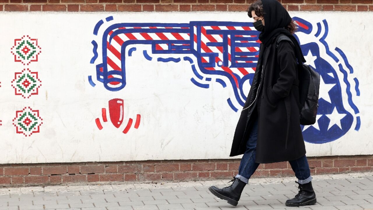 An Iranian woman walks past an anti-US mural on a wall outside the former US embassy in Tehran