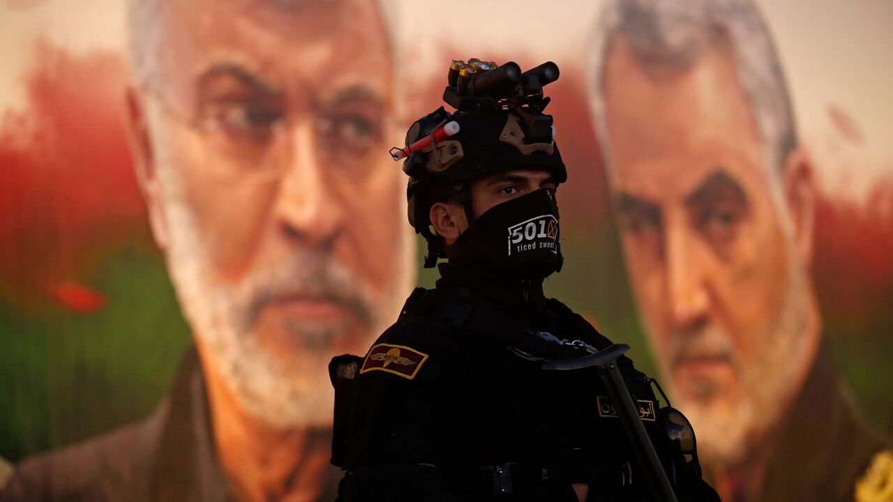 A member of Iraq's Hashed al-Shaabi stands guard in front of a banner depicting slain Iraqi commander Abu Mahdi al-Muhandis (L) and Iranian Revolutionary Guards commander Qasem Soleimani, near Baghdad's International Airport on January 2, 2023. (Photo by AHMAD AL-RUBAYE/AFP via Getty Images)