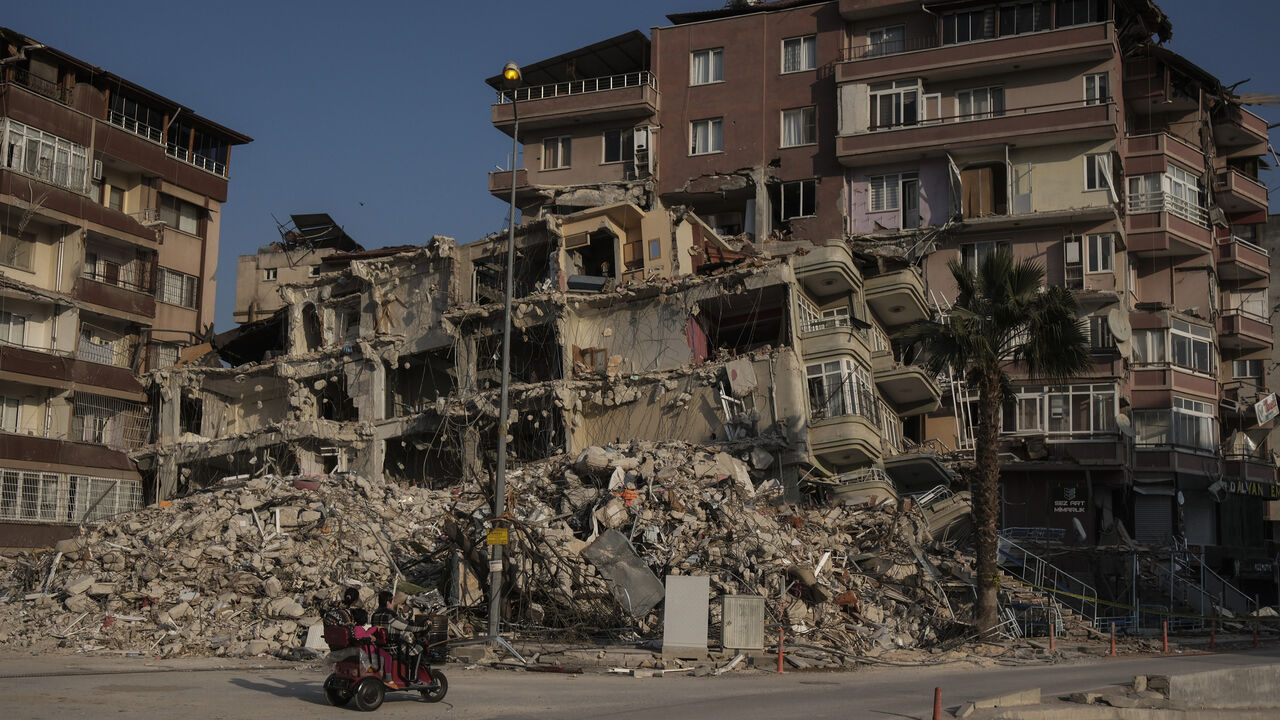 A family pass by a ruined building in Hatay, Turkey, Feb. 25, 2023.