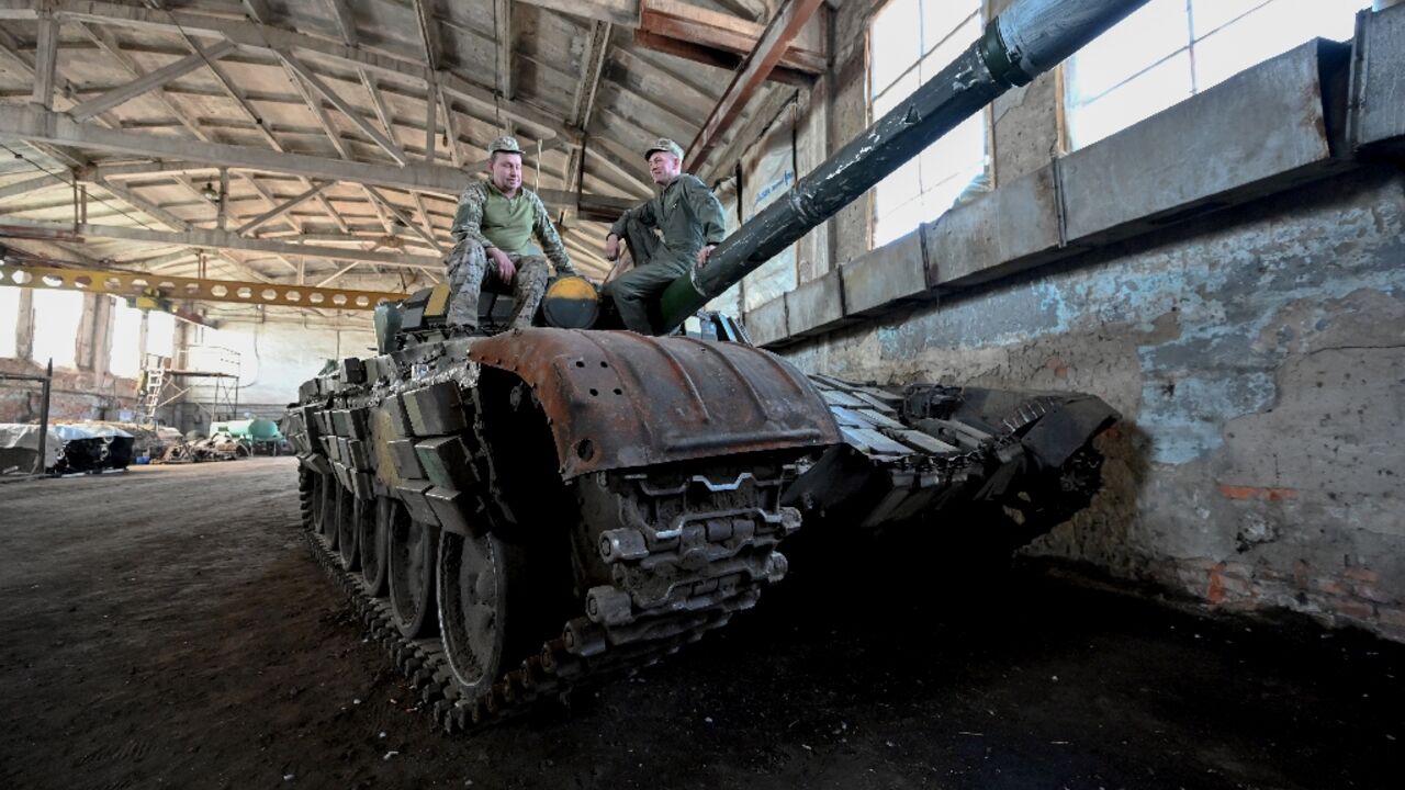 Ukrainian soldiers sit on a tank in a workshop of the repair battalion of the 3rd Tank Brigade repair an armoured vehicle at a workshop in Kharkiv region on May 17, 2023