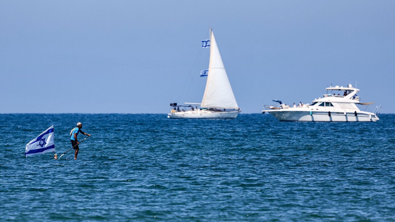 A man rows a stand-up paddle flying an Israeli flag near a sailing boat and a yacht in the Mediterranean sea off the coast of Tel Aviv on April 26, 2023, as Israel marks Independence Day (Yom HaAtzmaut), 75 years since the establishment of the Jewish state. (Photo by JACK GUEZ / AFP) (Photo by JACK GUEZ/AFP via Getty Images)