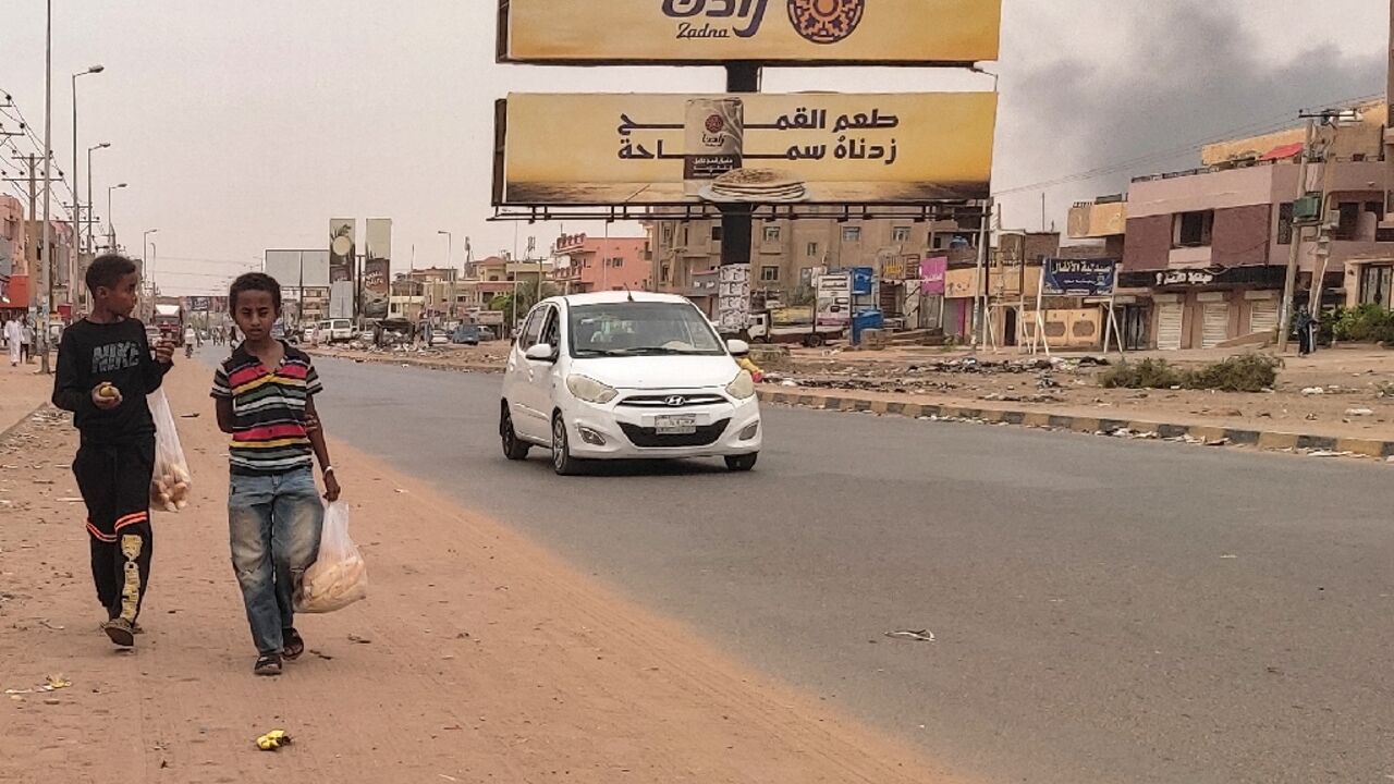 Smoke rises from nearby fighting as children take bags of bread home in Omdurman