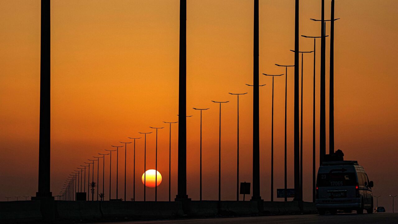 The sun sets behind road lamps along a highway in El-Shorouk.