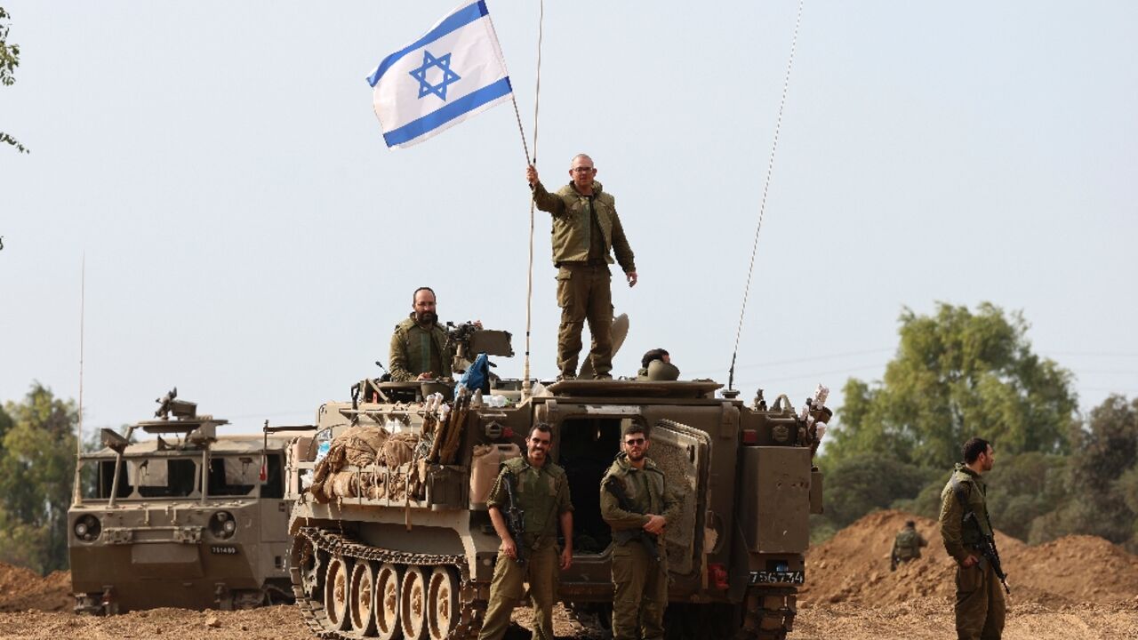 Israeli soldiers wave their national flag as they take positions in armoured vehicles near the border with Gaza in southern Israel