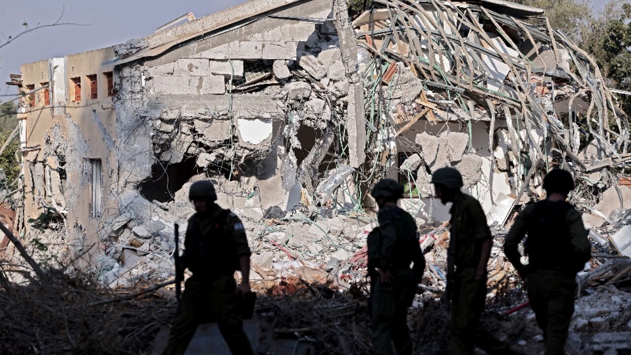 Israeli soldiers walk past a destroyed house in kibbutz Beeri 