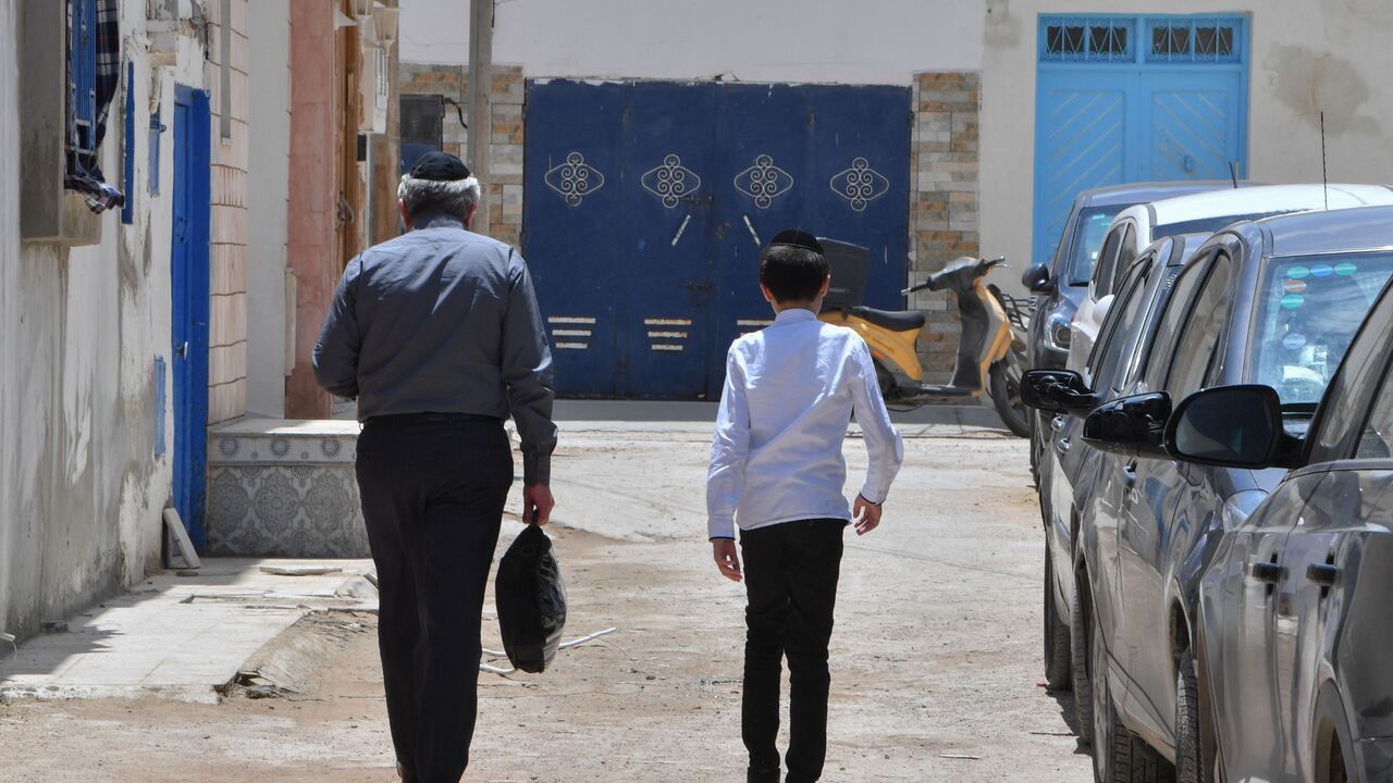 A Jewish man and a child walk through the Hara Kebira, the main Jewish quarter in the resort island of Djerba, near the Ghriba synagogue following a shooting spree by a police officer on the southern Tunisian island on May 10, 2023. Tunisian authorities were investigating the shootings that claimed five lives and sparked mass panic during a Jewish pilgrimage at Africa's oldest synagogue today. (Photo by FETHI BELAID / AFP) (Photo by FETHI BELAID/AFP via Getty Images)