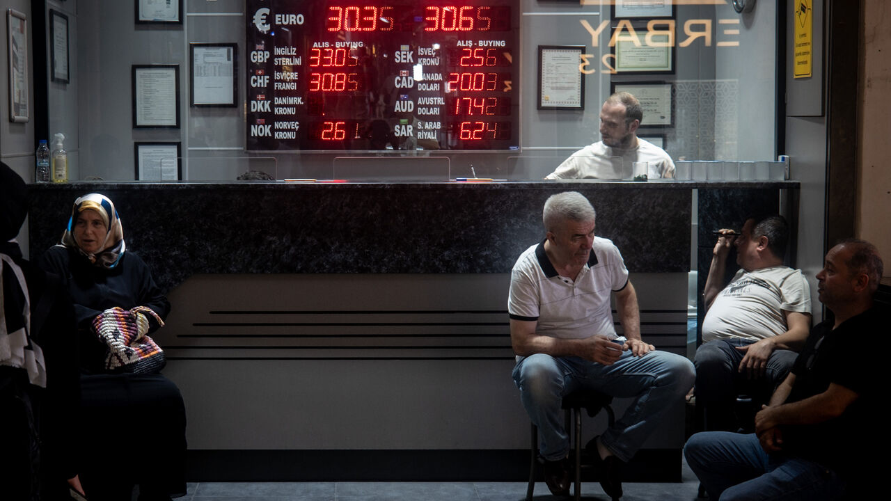 People sit in front of a currency exchange office on July 19, 2023 in Istanbul, Turkey.