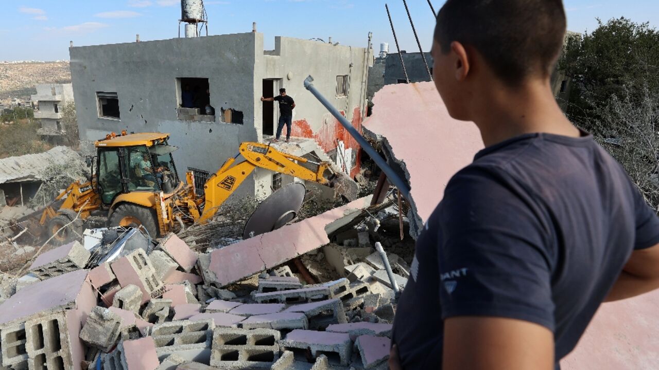 Palestinians look on as an excavator clears the rubble of the West Bank home of exiled Hamas number two Saleh al-Aruri after it was demolished by Israeli forces