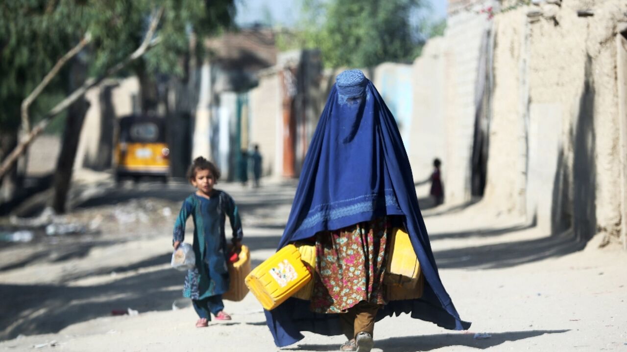 An Afghan woman carries canisters to fetch drinking water in Jalalabad on October 4, 2023