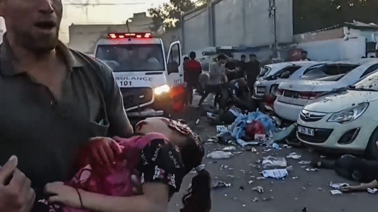 In this image grab taken from an AFPTV video footage shows a man carrying an injured girl near an ambulance damaged in a reported Israeli strike in front of Al-Shifa hospital in Gaza City on November 3, 2023