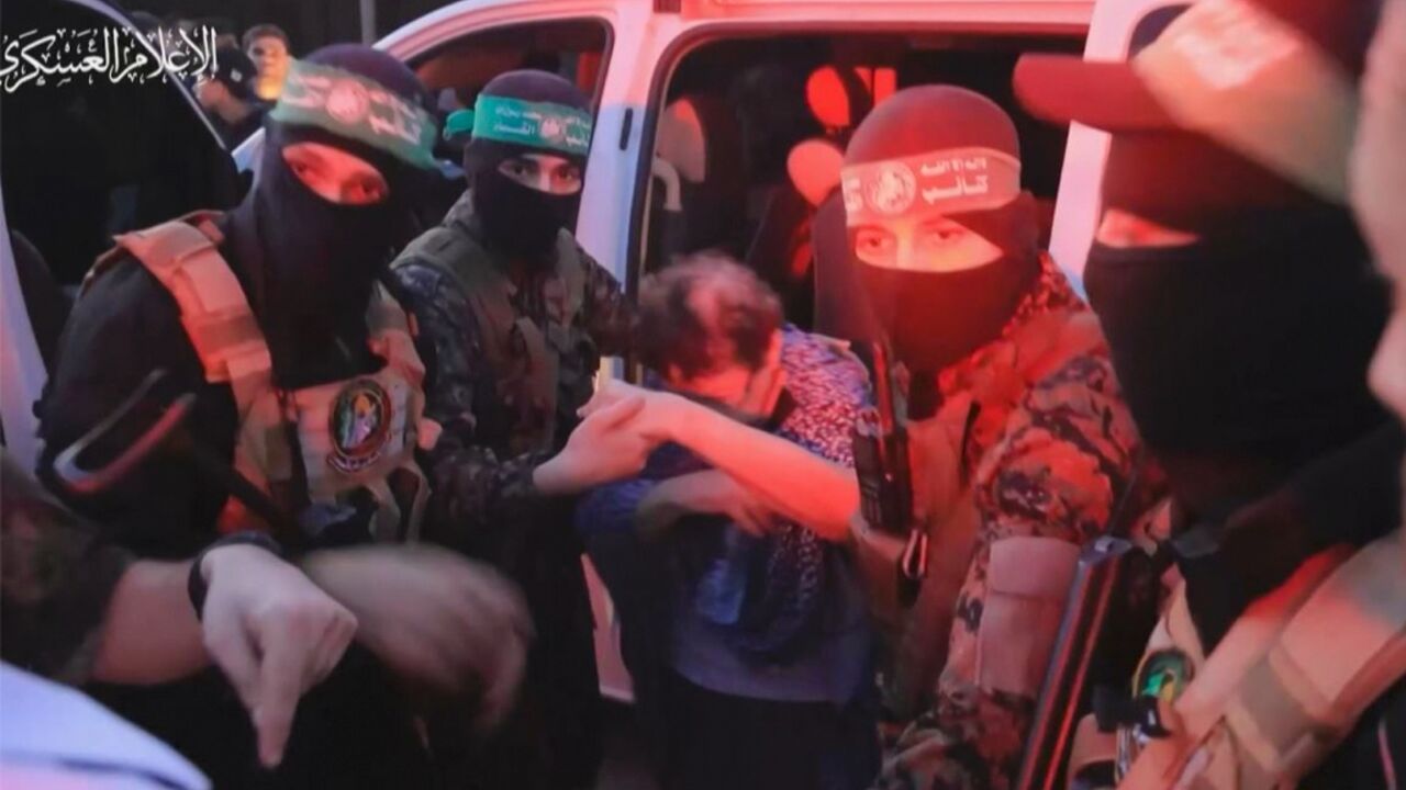 A member of Hamas' Al-Qassam Brigades helps a hostage out of a car before handing them over to officials from the International Committee of the Red Cross in Gaza